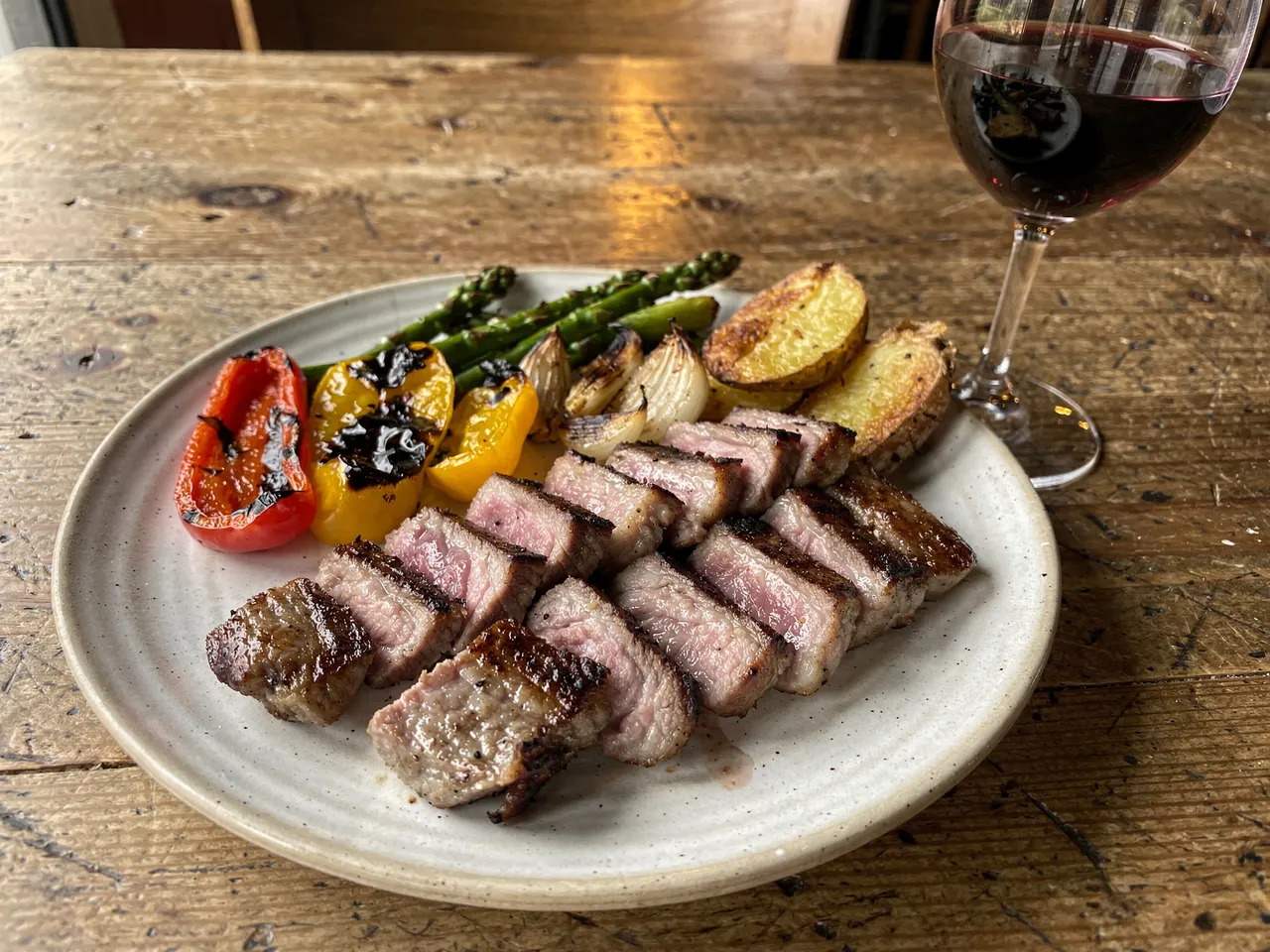 Carne a la brasa de encina cortada en tiras, con verduras asadas y una copa de vino tinto, servida en Taberna Los Aljibes