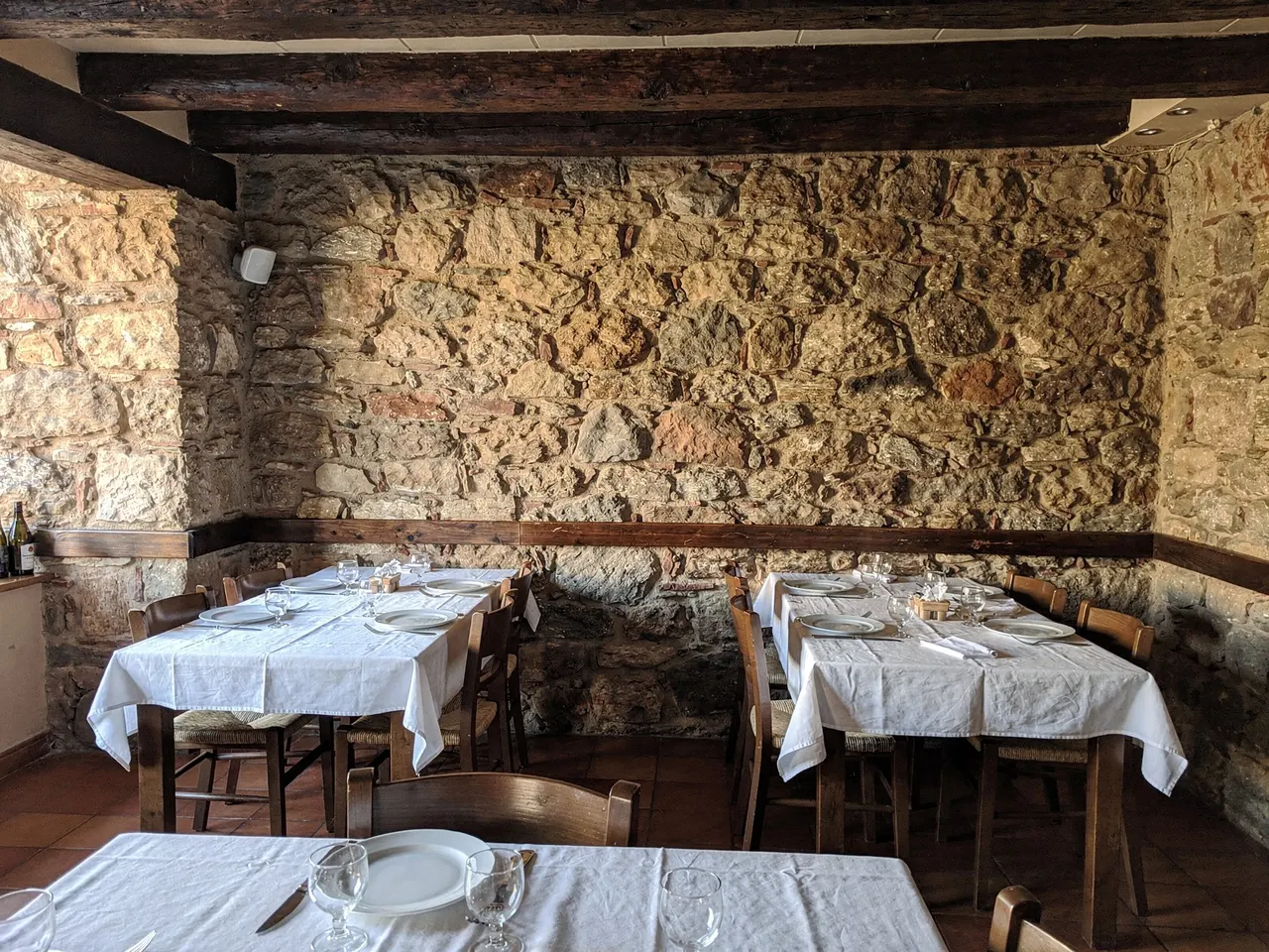 Comedor con muro de piedra, vigas de madera y mesas montadas