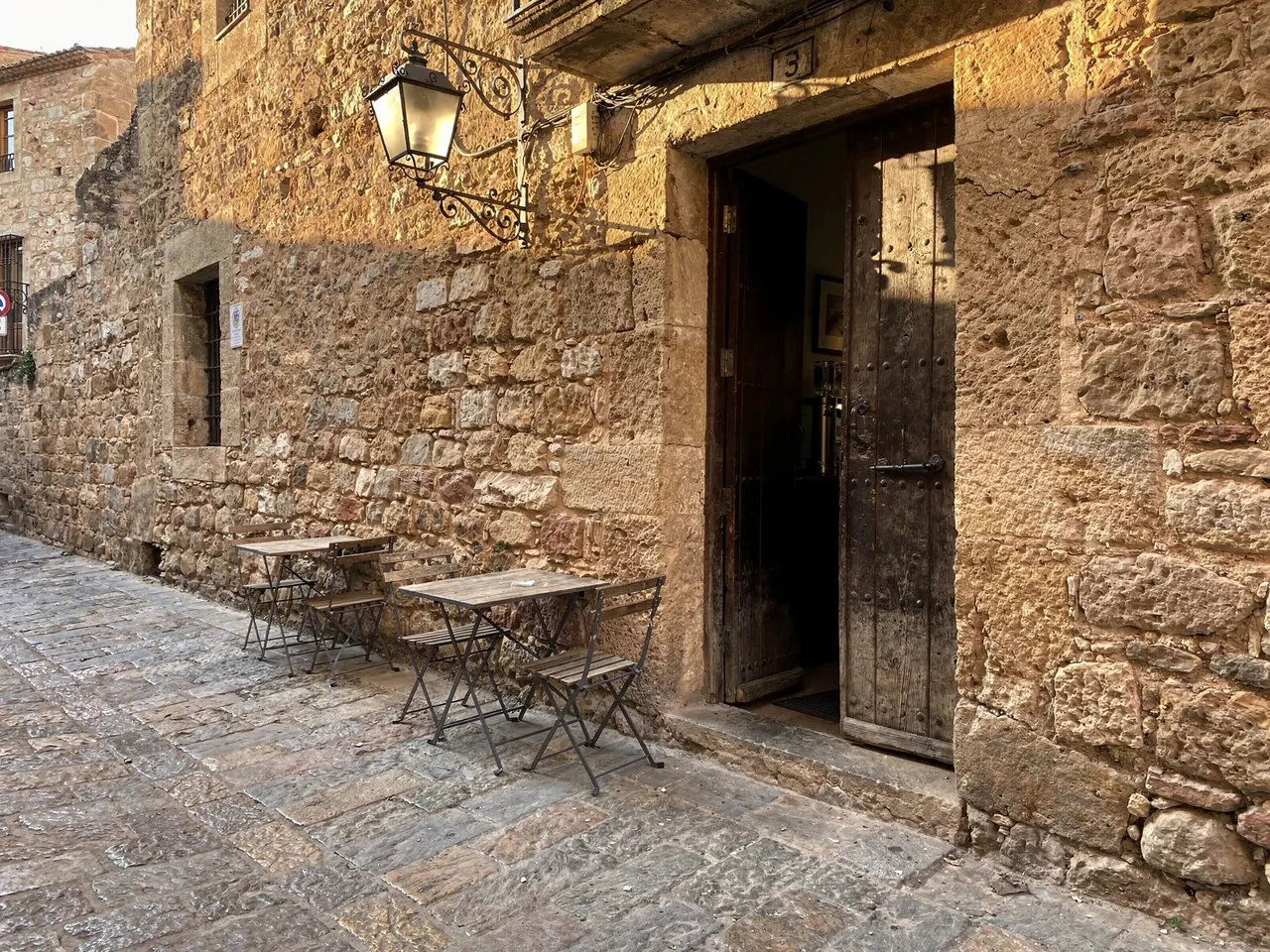 Fachada de piedra de la taberna con farol, puerta de madera y mesas fuera